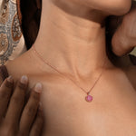 Load image into Gallery viewer, A close-up of a model wearing a delicate rose gold necklace. The round pendant, encrusted with sparkling pink pavé gemstones, rests elegantly against her skin, showcasing this beautiful piece of fashion jewellery.
