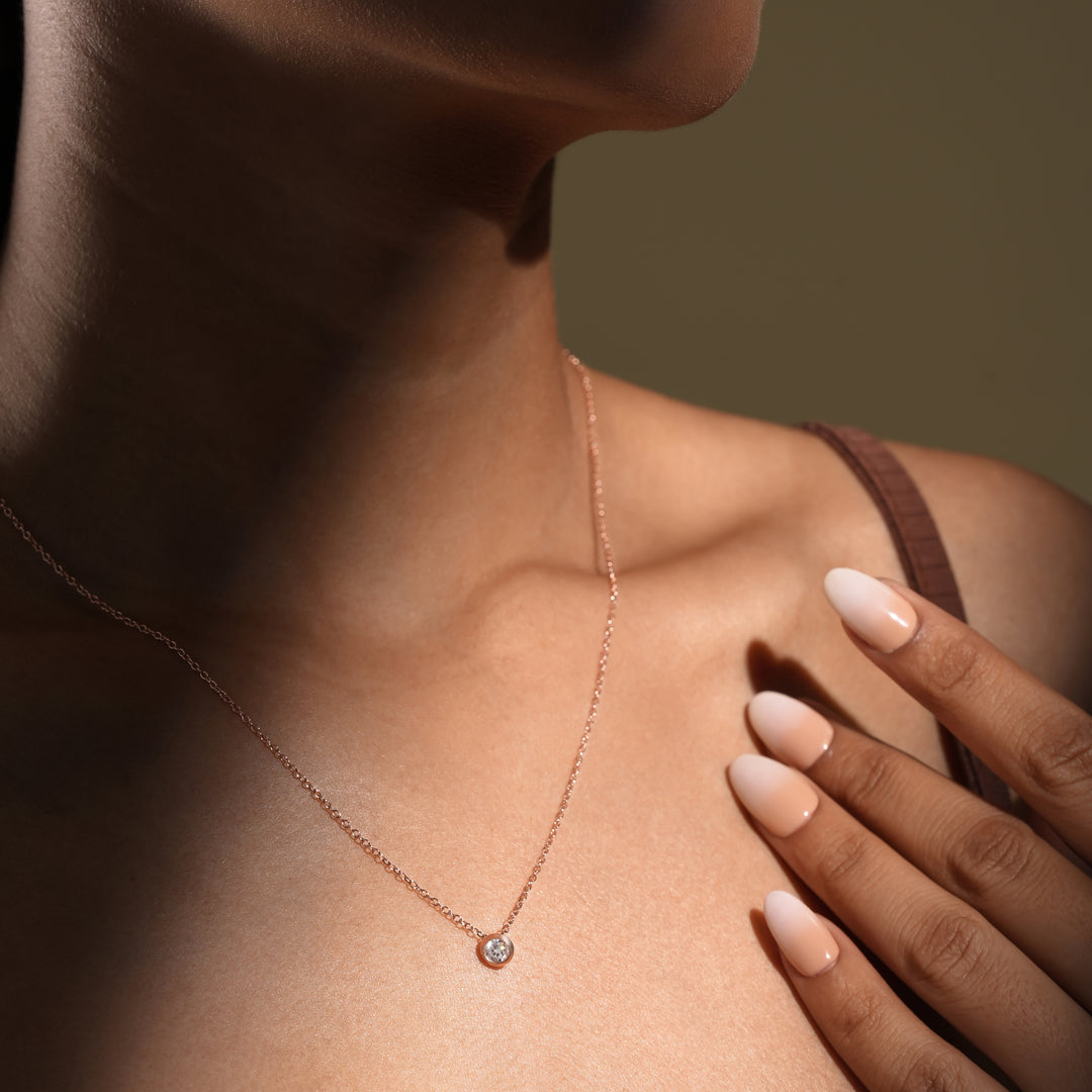 Necklace with a small round pendant worn by a person, with a hand touching the shoulder.