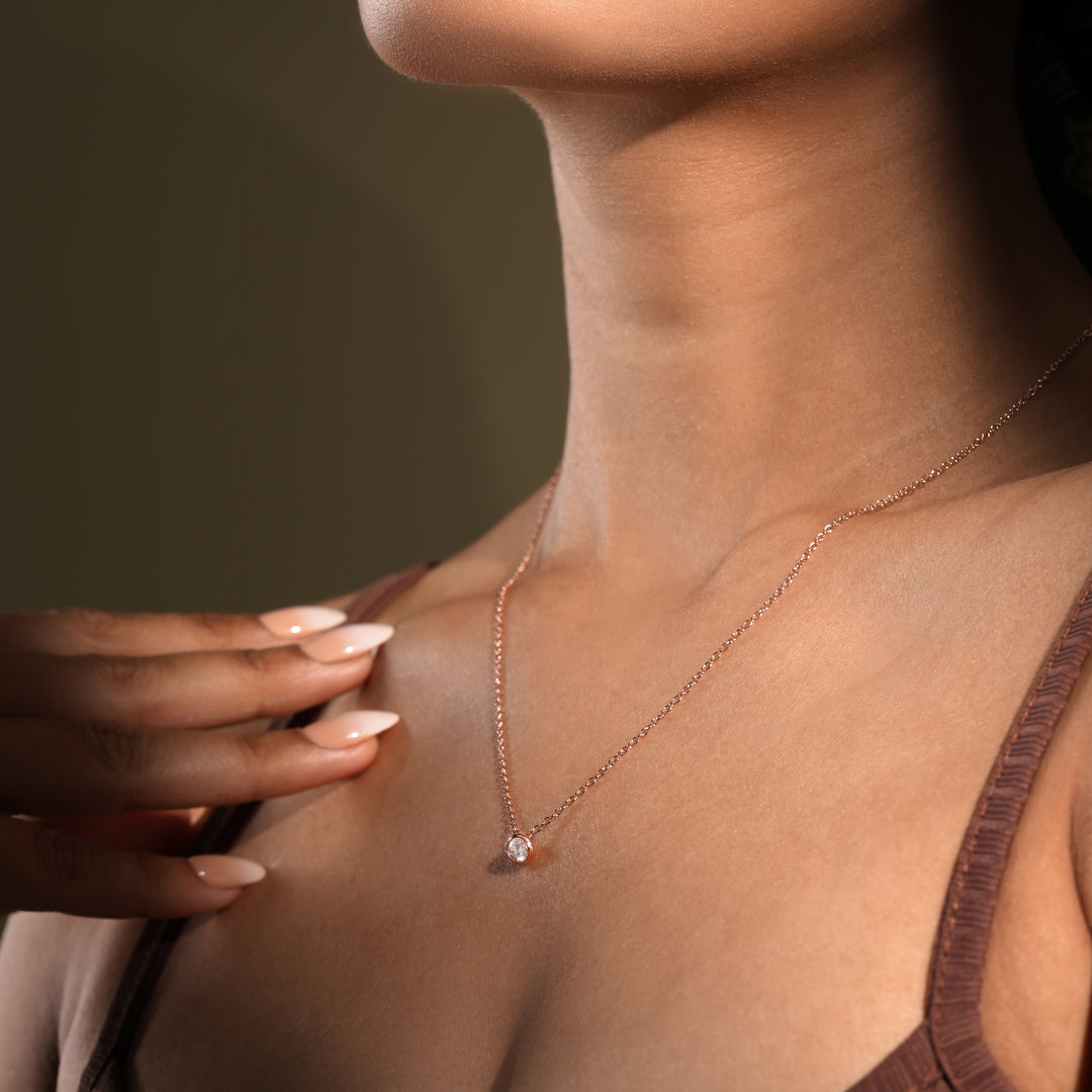 A close-up of a model wearing a delicate rose gold solitaire necklace from Zewory Jewellery. The minimalist, bezel-set crystal pendant sparkles against her skin, showcasing a timeless and elegant accessory perfect for any occasion.