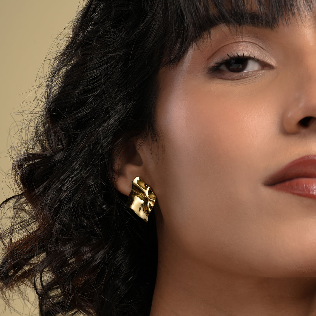 Close-up of a woman wearing a gold earring with a neutral background