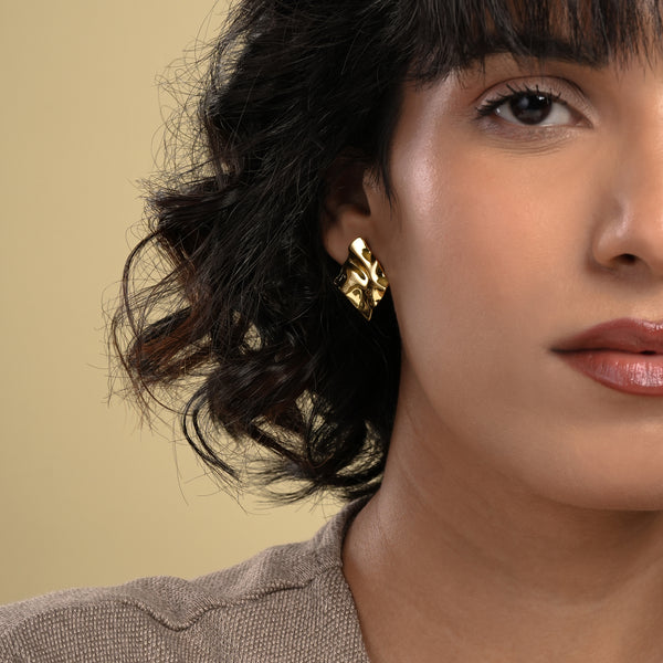 A close-up of a model wearing a bold, sculptural gold stud earring from Zewory Jewellery. The modern, wavy design makes a statement on her ear, showcasing a unique piece of artistic fashion jewellery.