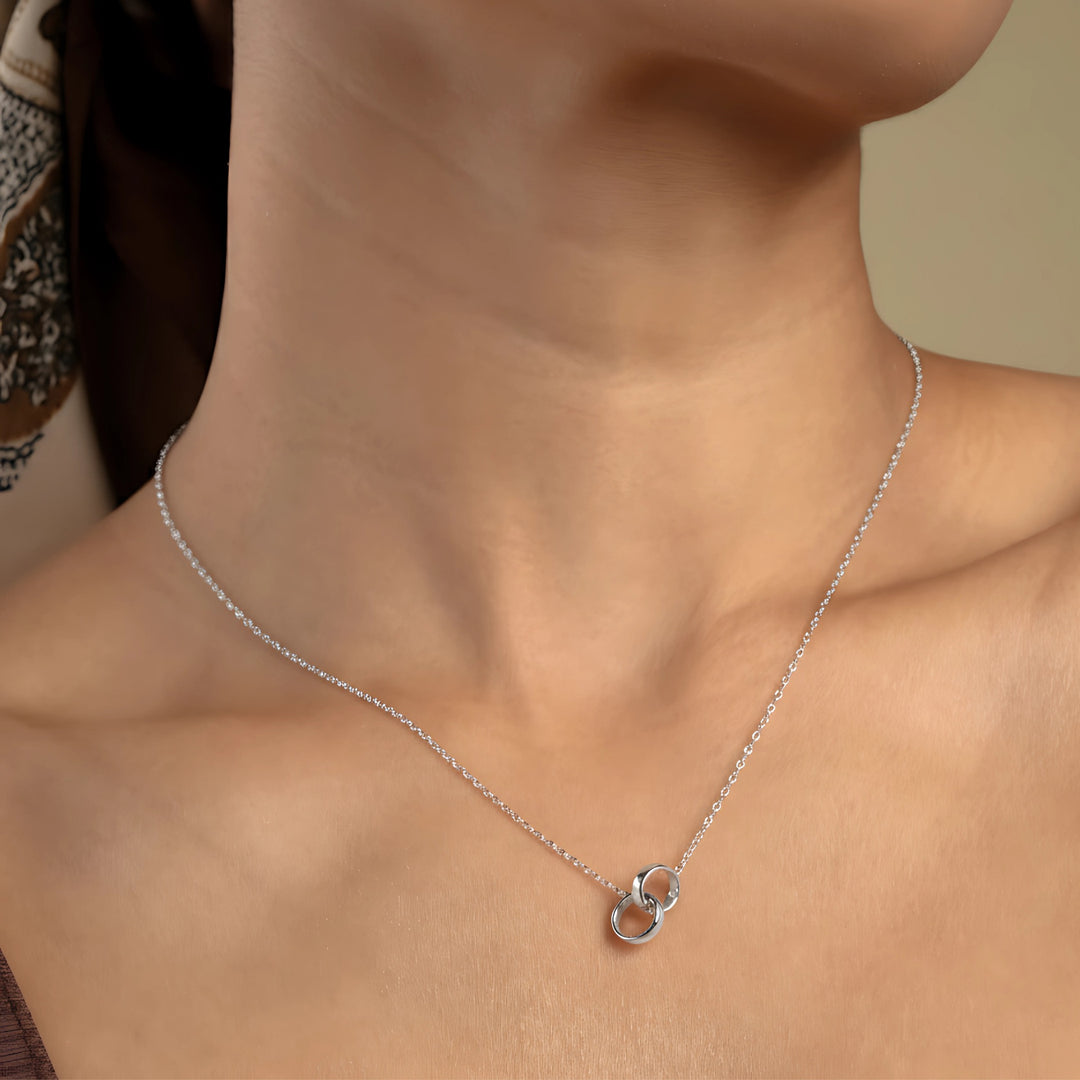 A close-up of a model wearing a delicate rose gold necklace with a symbolic interlocking rings pendant. The minimalist double-circle design sits elegantly against her skin, showcasing a timeless and meaningful piece of fashion jewellery.