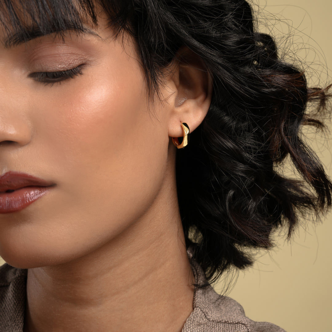 Close-up of a woman wearing a gold hoop earring with a neutral background