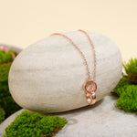 Load image into Gallery viewer, An elegant rose gold necklace from Zewory Jewellery, featuring a delicate double interlocking rings pendant. This minimalist piece is displayed on a smooth, light-grey stone surrounded by vibrant green moss for a natural and serene product shot.
