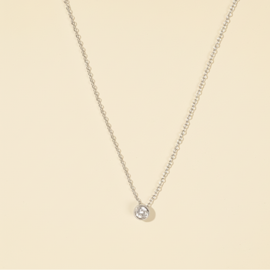 Delicate silver necklace with a small round pendant on a beige background