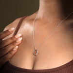 Load image into Gallery viewer, A close-up of a model wearing an elegant two-tone interlocking hearts necklace from Zewory Jewellery. The romantic pendant, featuring a large silver open heart and a smaller rose gold open heart, rests gracefully against her skin.

