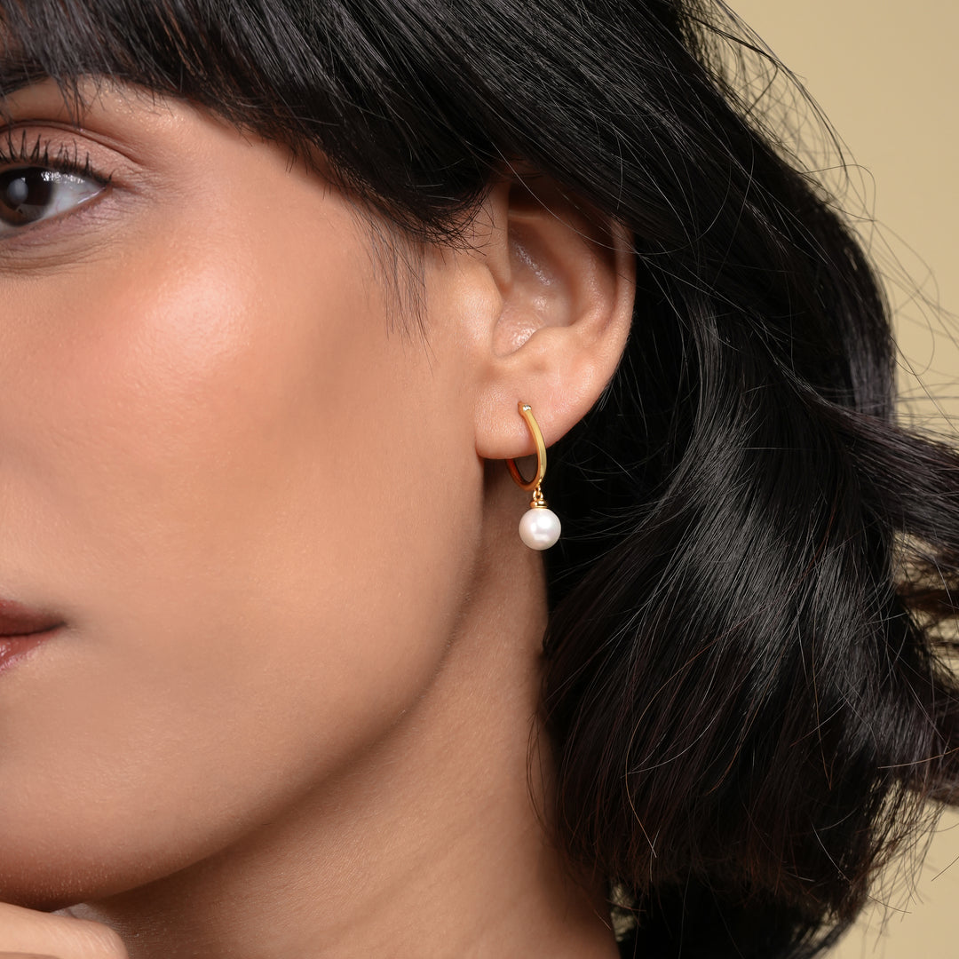 Close-up of a woman wearing a pearl earring with a neutral background