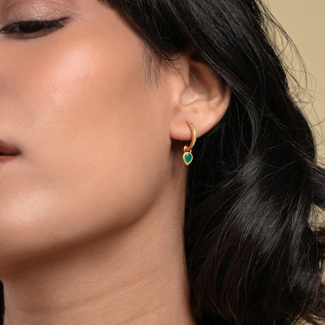 Close-up of a person wearing a gold hoop earring with a green gemstone.