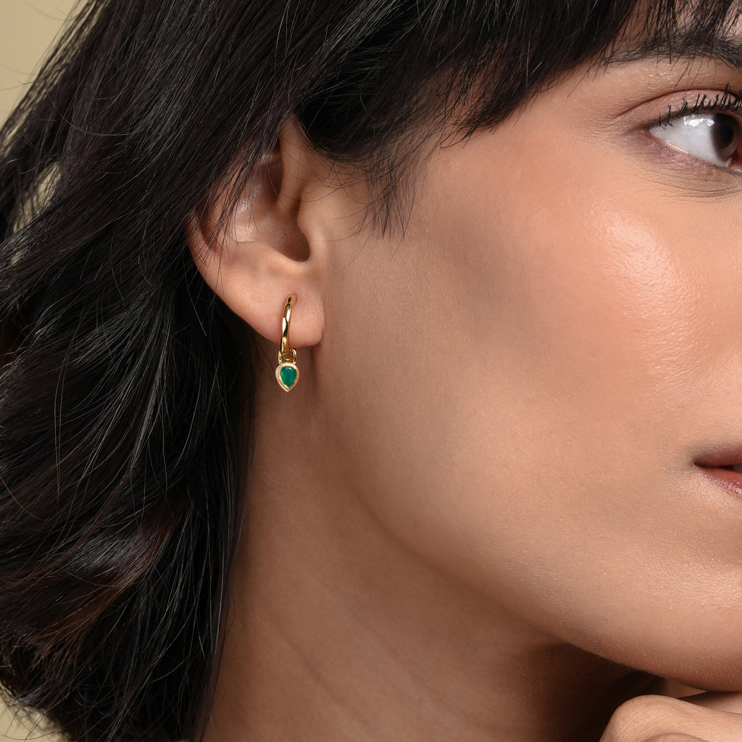 Close-up of a woman wearing gold hoop earrings with green gemstones.