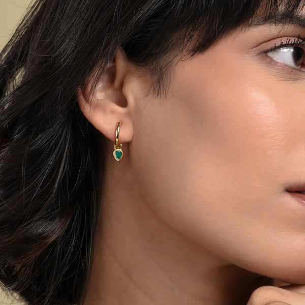 Close-up of a woman wearing gold hoop earrings with green gemstones.