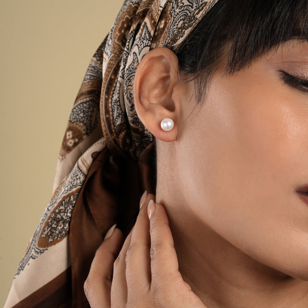 Close-up of a woman wearing a pearl earring with a patterned headscarf on a beige background