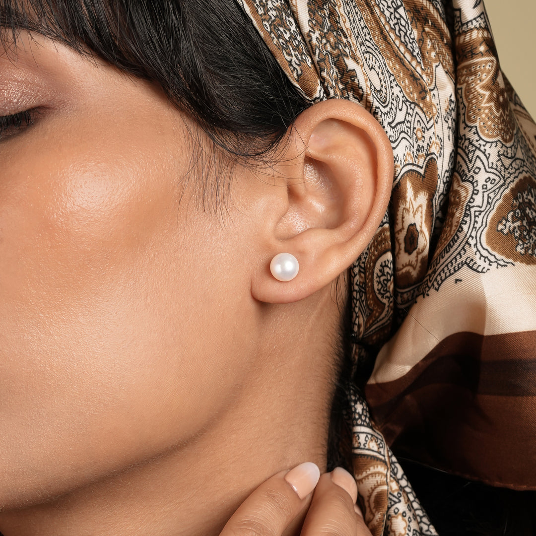 Close-up of a woman wearing a pearl earring with a patterned headscarf in the background.